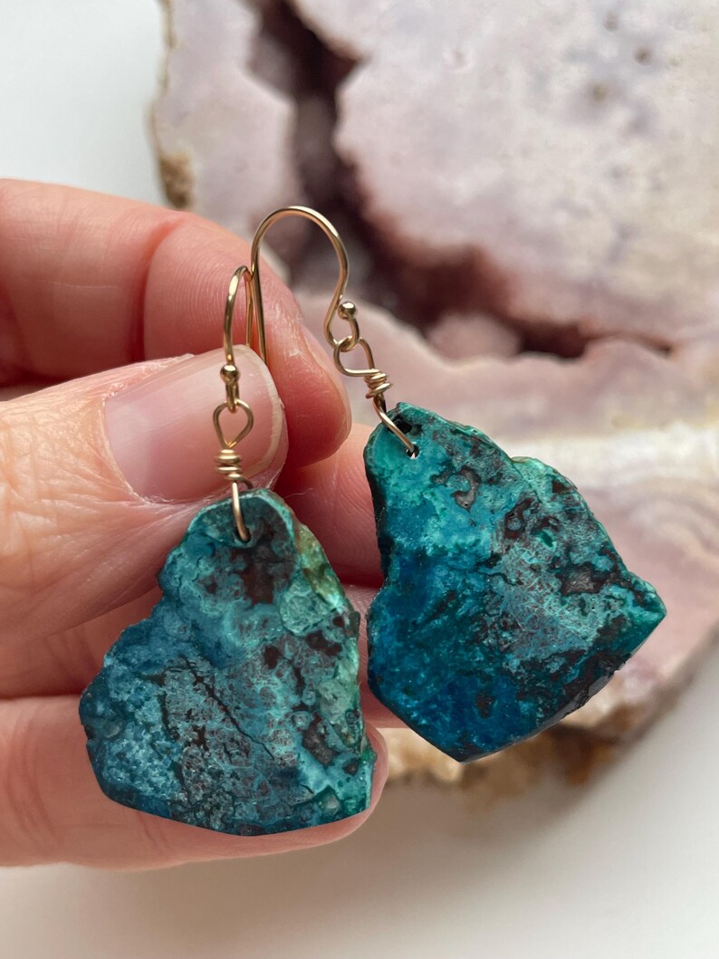 May include: A pair of turquoise green gemstone earrings with gold wire wrapped around the stones and gold hooks. The stones have a rough, natural texture.