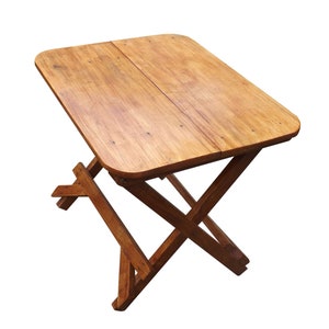 May include: A wooden folding table with a natural brown finish. The table has a rectangular top and a simple, sturdy X-shaped base.