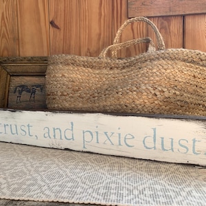 Puede incluir: Un letrero de madera blanco con bordes pintados de negro y letras azules que dice "and trust, and pixie dust".