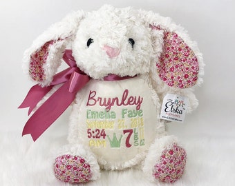 May include: A white plush bunny rabbit with floral patterned ears and feet. The bunny has a pink nose and a dark pink ribbon around its neck. The bunny has embroidered text that reads "Brynley, Emelia Faye, September 27, 2018, 5:24 AM, 7 lbs 5 oz."
