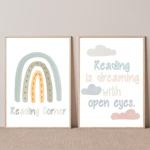 Puede incluir: Dos impresiones enmarcadas con fondo blanco. La impresión de la izquierda presenta un arcoíris con colores verde, azul y naranja y el texto "Reading Corner". La impresión de la derecha presenta un texto azul y amarillo que dice "Reading is dreaming with open eyes." y tres nubes en rosa, azul y gris.
