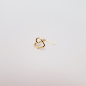 May include: A gold heart-shaped nose ring with a curved post.