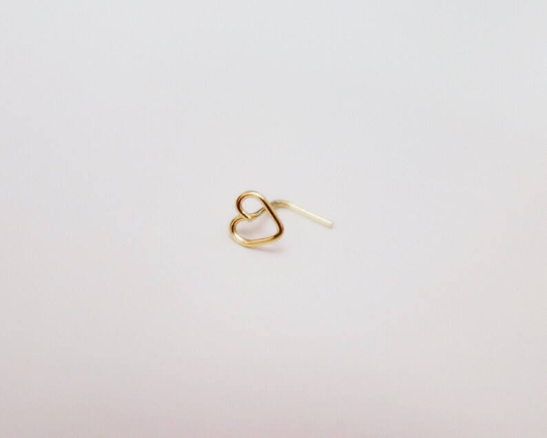 May include: A gold heart-shaped nose ring with a curved post.