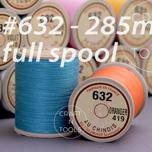 May include: A full spool of turquoise thread labeled "632 - Lichen 298" and a full spool of orange thread labeled "632 - Oranger 419". Both spools are labeled "Au Chinois" and "Fabrique en France". The spools are surrounded by other spools of thread in various colors.