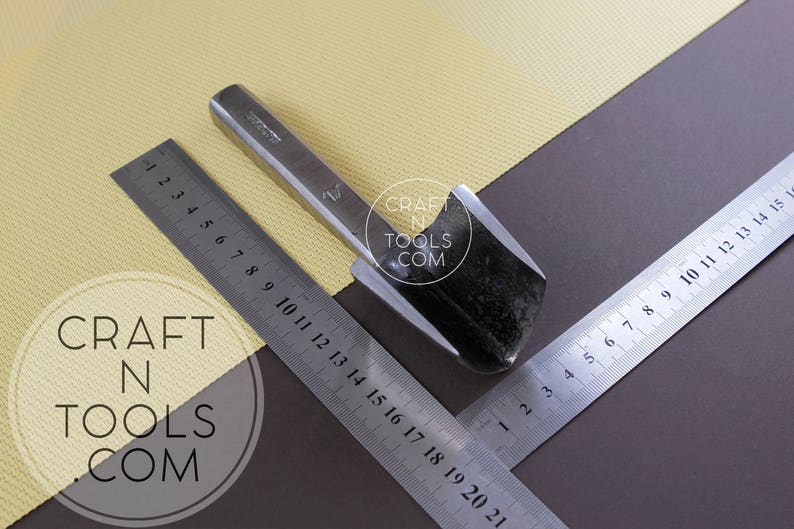 Puede incluir: Un primer plano de una herramienta de trabajo del cuero de metal con una cuchilla curva. La herramienta est&aacute; sobre una superficie amarilla con una regla marcada en cent&iacute;metros. El texto "CRAFT N TOOLS COM" es visible en la imagen.