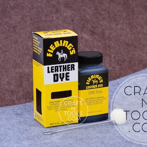 May include: A bottle of Fiebing's Leather Dye in USMC Black, a 4 fl oz (118 ml) bottle with a yellow and black label. The bottle is next to a box of Fiebing's Leather Dye, also in USMC Black, with a yellow and black label. The box is 4 fl oz (118 ml).