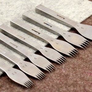 May include: Set of eight silver leather stitching tools with different sized prongs. The tools are labeled with the number of prongs, ranging from 1 to 8.