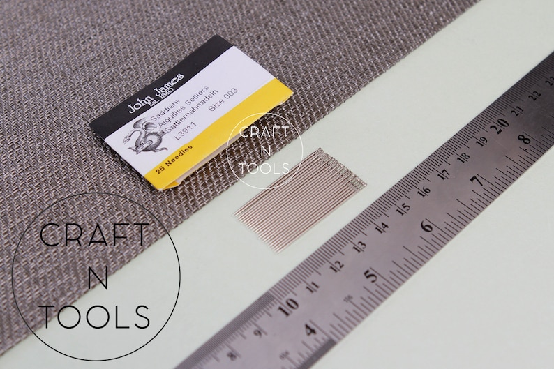 May include: A pack of 25 John James Saddlers needles, size 003, with a yellow and black label. The needles are laid out on a white surface next to a ruler.