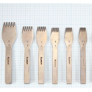 May include: Set of eight leather stitching tools with different sized prongs. The tools are made of metal and have a silver finish. The tools are labeled with numbers 5, 6, 7, 8, 9, 10, and 12. The tools are arranged in a row on a grid background.