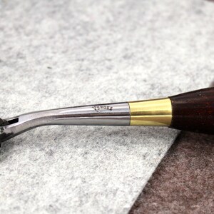 May include: A silver and brass leather stitching tool with a wooden handle. The tool has a star-shaped wheel and the text "VERGEZ" is engraved on the metal.
