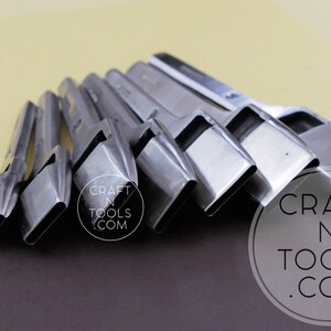 May include: A set of silver-colored leathercraft tools arranged in a row. The tools have a rectangular shape with a beveled edge. The background is a mix of brown and yellow.