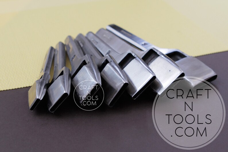 May include: A set of silver-colored leathercraft tools arranged in a row. The tools have a rectangular shape with a beveled edge. The background is a mix of brown and yellow.