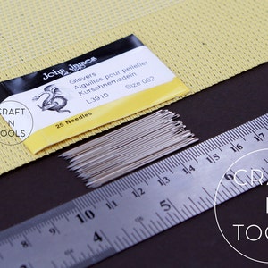 May include: A pack of 25 silver needles for glove making, labelled "John James Glovers Aiguilles pour pelletier Kurschnernadeln L3910 Size 002 25 Needles" and "CRAFT N TOOLS". The needles are laid out next to a ruler, measuring 25.4 cm.