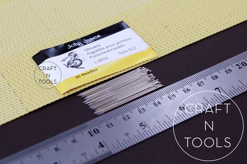 May include: A pack of 25 silver needles for glove making, labelled "John James Glovers Aiguilles pour pelletier Kurschnernadeln L3910 Size 002 25 Needles" and "CRAFT N TOOLS". The needles are laid out next to a ruler, measuring 25.4 cm.