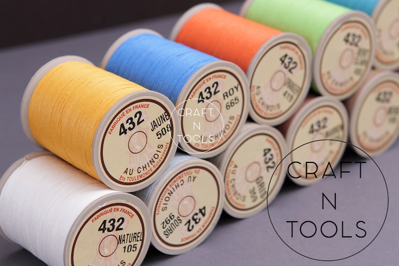 May include: Close-up of spools of thread in various colors, including yellow, blue, orange, green, and white. Each spool has a label with the number 432 and a description in French. The label also includes the text "CRAFT N TOOLS".