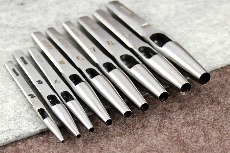 K&ouml;nnte beinhalten: Ein Satz von acht silbernen Lederlocher aus Metall in verschiedenen Gr&ouml;&szlig;en von 2 bis 8 mm. Die Locher sind nach Gr&ouml;&szlig;e geordnet, der kleinste links und der gr&ouml;&szlig;te rechts.