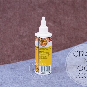 May include: A clear bottle of Leathercraft  Leather Cement with a yellow label. The label has a picture of a horse and the text "Leathercraft Cement" and "High strength bonding for leather, vinyl, shellac and paper crafts".