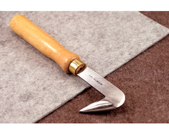 May include: A wooden handled leather working tool with a curved metal blade and a pointed tip. The blade is marked "T.L. MEZIP".