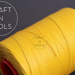 Puede incluir: Una bobina de hilo encerado amarillo brillante. El hilo est&aacute; enrollado apretado y tiene una textura lisa y uniforme. La bobina est&aacute; etiquetada con "CRAFT N TOOLS".