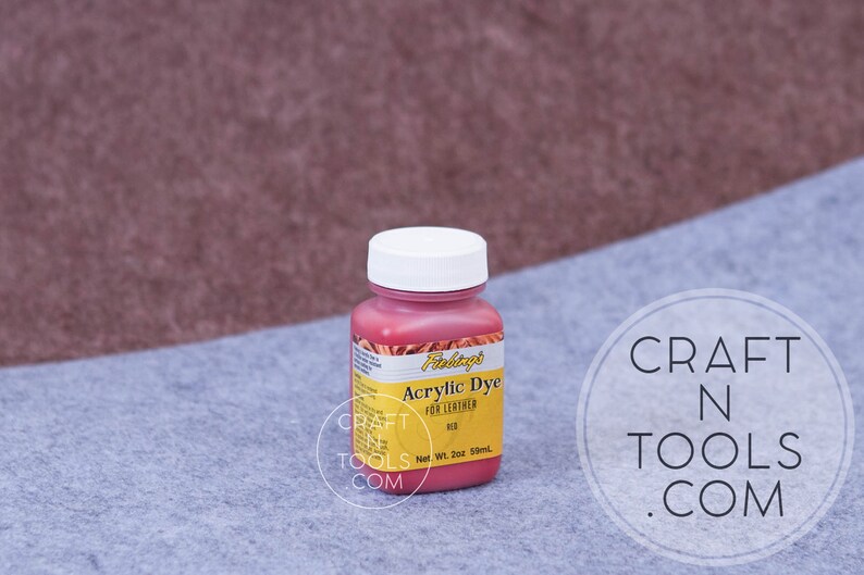 May include: A small bottle of Fiebing's Acrylic Dye for Leather in red. The bottle is labeled with the brand name, product name, and color. The bottle is sitting on a gray surface.