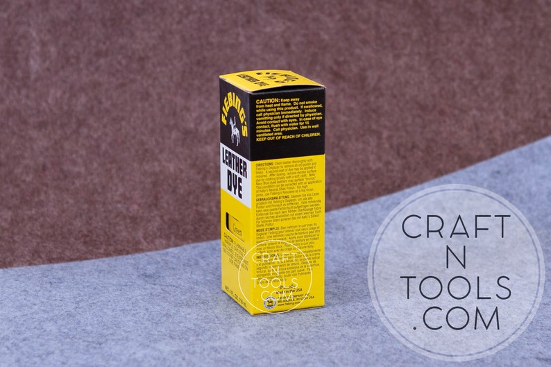 May include: A yellow and black bottle of Fiebing's Leather Dye. The bottle is labeled with the product name, color, and instructions for use. The bottle is sitting on a gray surface.