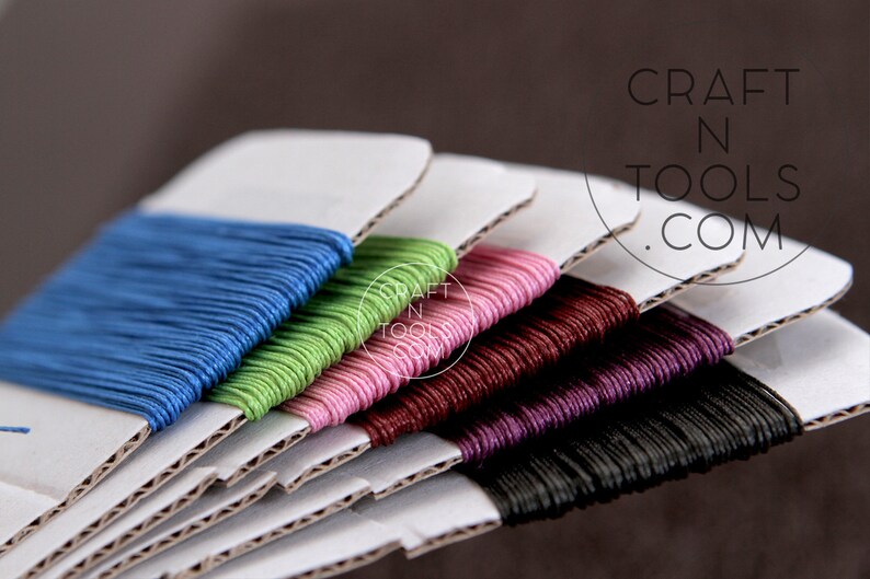 May include: A set of six spools of waxed cotton cord in various colors, including blue, green, pink, burgundy, purple, and black. The spools are stacked on top of each other and labeled "CRAFT N TOOLS .COM".
