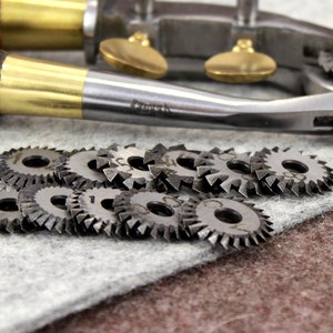 May include: A set of metal rotary blades for a leather crafting tool. The blades are circular with serrated edges and have numbers on them. The blades are on a gray surface.