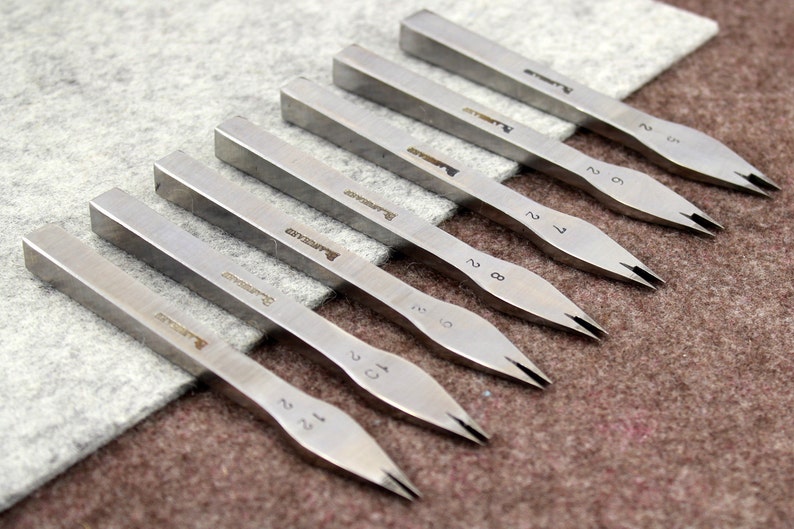 May include: A set of eight silver metal tools with pointed tips and numbered handles. The tools are arranged in a row on a gray fabric surface.