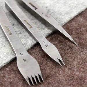 May include: Three metal leather stitching tools with different sized prongs. The tools are labeled "2.8", "5.8", and "C".