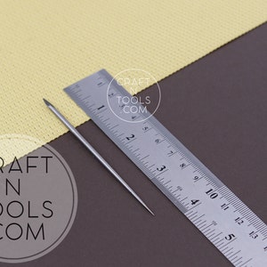 May include: A silver metal needle tool with a pointed tip, measuring approximately 4 inches in length, is placed on a brown surface next to a silver ruler. The ruler is marked with inches and fractions of an inch. The text "CRAFT N TOOLS .COM" is visible in the lower left corner of the image.