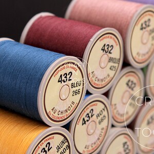 May include: Close-up of spools of thread in various colors, including blue, red, yellow, and brown. Each spool has a label with the number "432" and the color name in French. The label also includes the text "Au Chinois" and "Fabrique en France".