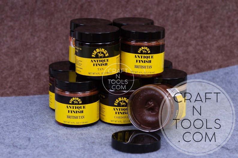 May include: Multiple jars of Fiebing's Antique Finish leather dye in various colors, including Tan, British Tan, and Cordova. The jars are stacked on a gray surface. The text "CRAFT N TOOLS .COM" is visible in the background.