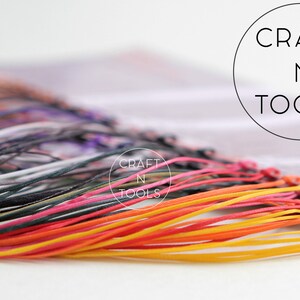 May include: A close-up of a variety of colorful cords, including yellow, orange, red, pink, black, and gray. The cords are arranged in a fan shape and are tied together at the top. The text "CRAFT N TOOLS" is visible in the background.