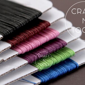 May include: Six spools of embroidery floss in various colors, including black, burgundy, pink, purple, green, and blue, are stacked on top of each other. The spools are labeled "CRAFT N TOOLS".