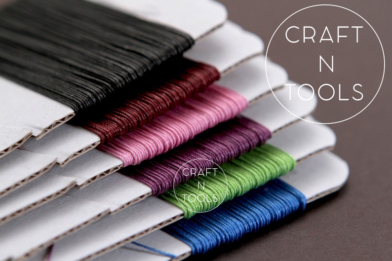 May include: Six spools of embroidery floss in various colors, including black, burgundy, pink, purple, green, and blue, are stacked on top of each other. The spools are labeled "CRAFT N TOOLS".