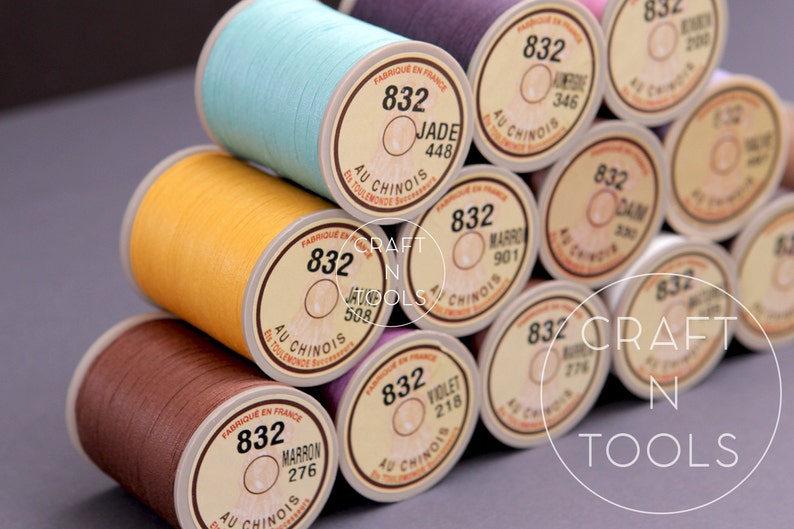 May include: A close-up of a stack of spools of thread in various colors, including teal, yellow, brown, purple, and pink. The spools are labeled with the number "832" and the color name in French. The text "CRAFT N TOOLS" is visible in the lower right corner of the image.