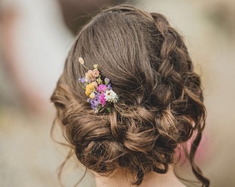 Puede incluir: Una mujer con cabello castaño peinado en un moño suelto con un pequeño grupo de flores secas metidas en un lado.