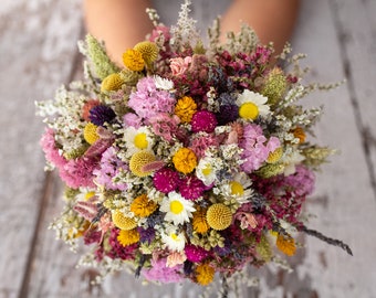 Könnte beinhalten: Ein Strauß getrockneter Blumen in den Farben Rosa, Lila, Gelb und Weiß. Der Strauß besteht aus verschiedenen Blumensorten, darunter Gänseblümchen, Lavendel und Wildblumen.