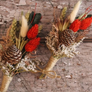 May include: Two small bouquets of dried flowers with pine cones, wheat, and red flowers. The bouquets are tied with twine.