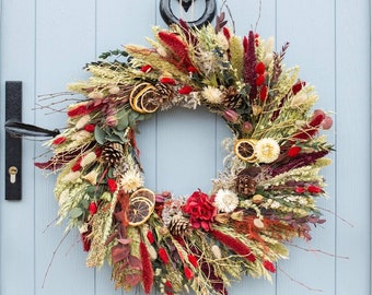 May include: A dried floral wreath with red, orange, and white flowers, dried grasses, and pine cones. The wreath is hanging on a light blue door.