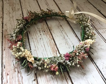 May include: A floral crown made with dried flowers in shades of white, pink, and green. The crown is tied with a white satin ribbon.