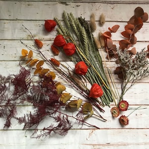 Puede incluir: Arreglo de flores secas con flores, hojas y hierbas rojas, naranjas y marrones. El arreglo incluye eucalipto seco, helecho y trigo.