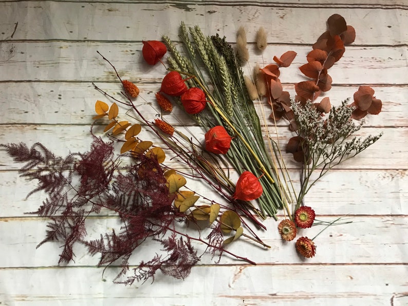Puede incluir: Arreglo de flores secas con flores, hojas y hierbas rojas, naranjas y marrones. El arreglo incluye eucalipto seco, helecho y trigo.