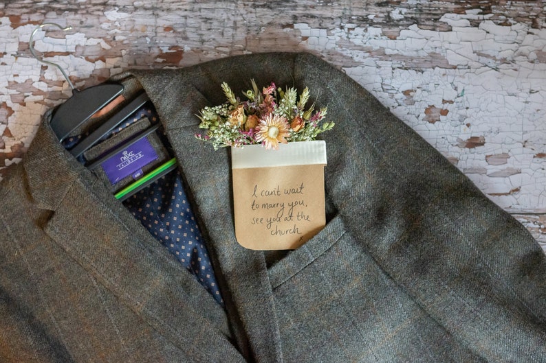 May include: A gray tweed jacket with a brown paper pocket square. The pocket square has dried flowers and a handwritten note that says "I can't wait to marry you, see you at the church."