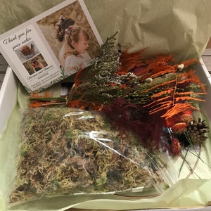 Puede incluir: Una caja blanca llena de arreglos florales secos, musgo y una tarjeta de agradecimiento. La tarjeta dice "Gracias por su pedido." y tiene una imagen de un arreglo floral.