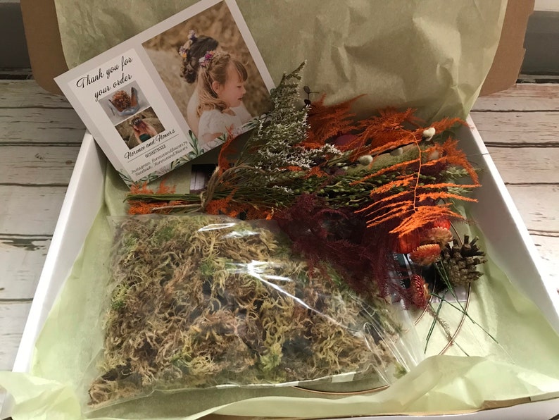 Puede incluir: Una caja blanca llena de arreglos florales secos, musgo y una tarjeta de agradecimiento. La tarjeta dice "Gracias por su pedido." y tiene una imagen de un arreglo floral.