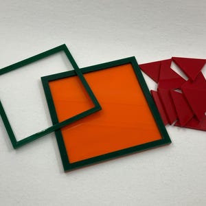 Op de afbeelding: Een verzameling geometrische vormen in levendige kleuren. Er zijn twee groen omkaderde vierkanten, één met een oranje centrum en de andere leeg. Er is ook een verzameling rode driehoeken aanwezig, wat wijst op een puzzel of educatief speelgoed.