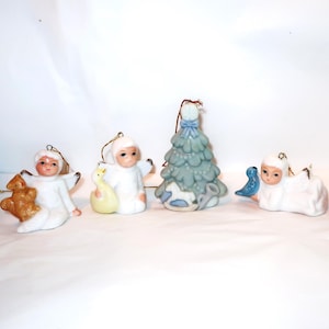 May include: A collection of ceramic Christmas ornaments. The ornaments include angel figures, a Christmas tree, and a red die. The angels are white with painted faces and hold various objects.