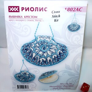 May include: A Riolis 1802AC cross stitch kit package featuring a blue and white shell-shaped pincushion design. The packaging displays the finished product in three views, including a hanging shell, a floral shell, and an open shell with a pearl.