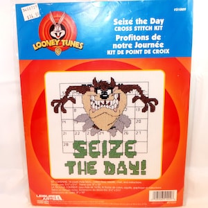 May include: A Looney Tunes cross stitch kit featuring Taz, the Tasmanian Devil, with the phrase "Seize the Day!" in green. The kit includes Aida fabric, floss, a needle, chart, and instructions. The design size is 5 1/2 x 5 1/2 inches, and the frame size is 8 x 10 inches.